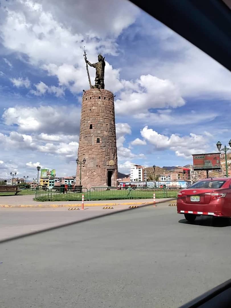 stone tower with a bronze statue of a man, as seen from a car window